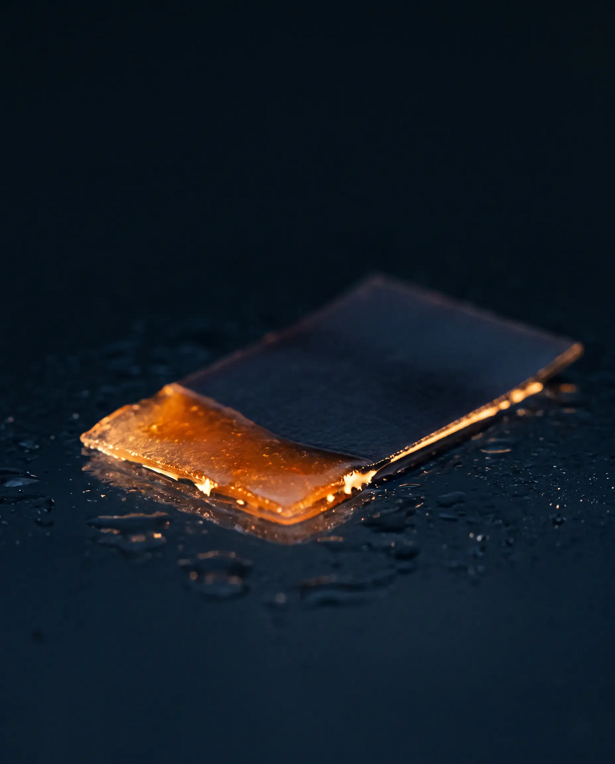 A strip dissolving on a dark wet surface, its edge glowing amber.